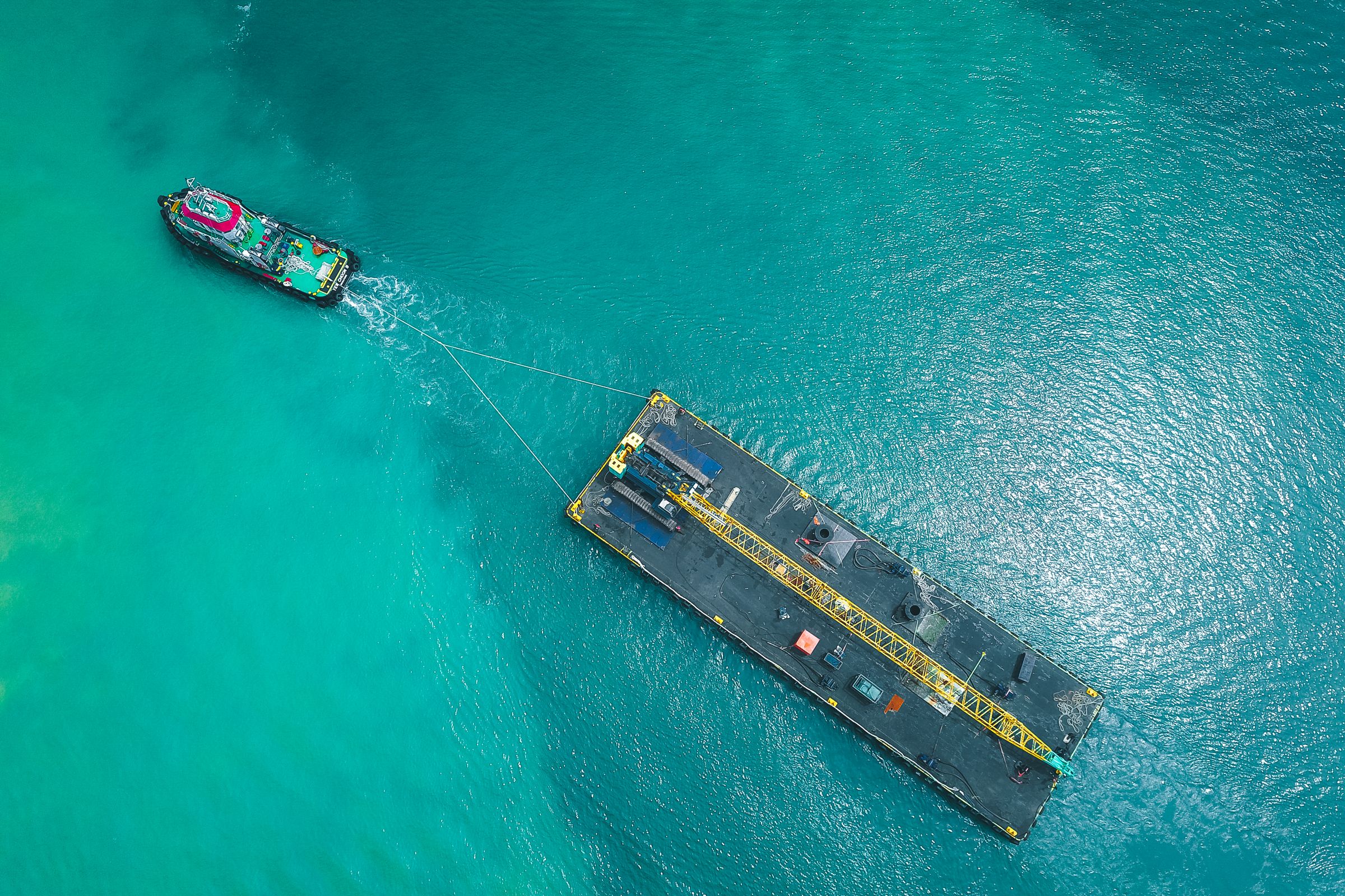 Tugboat pulling a large barge across a vivid blue sea